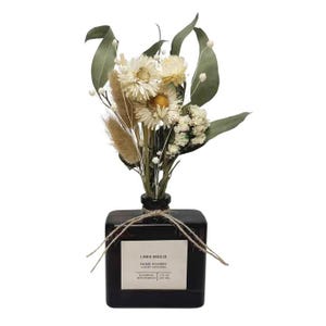 May include: A square dark amber glass diffuser bottle with a white label reading LINEN BREEZE HAND POURED LUXURY DIFFUSER BOTANICAL REED BUNDLES 7 FL OZ (207 ML) tied with twine, containing a bouquet of dried white flowers, green leaves, and tan grass.