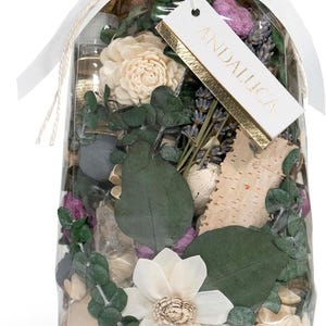May include: A clear plastic bag filled with potpourri, including dried flowers, leaves, and wood pieces. The bag is tied with a white ribbon and has a white tag with the word "ANDALUCIA" written in gold lettering.