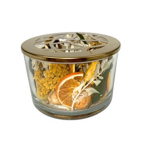 May include: A clear glass jar with a gold-colored metal lid featuring a decorative cutout design. The jar is filled with dried orange slices, yellow flowers, and other dried botanicals. The jar is a decorative home accent.