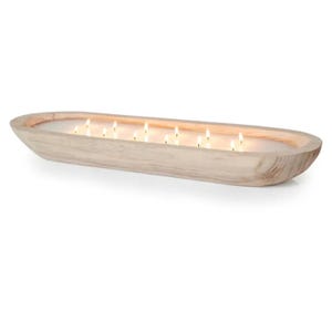 May include: A long, oval wooden bowl filled with a white candle. The candle has multiple wicks that are lit and burning.