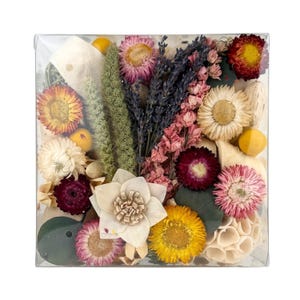 May include: A clear box filled with dried flowers and botanicals. The flowers are in shades of pink, purple, yellow, and white. There are also some dried leaves and twigs in the box.