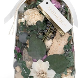 May include: A clear cellophane bag filled with dried flowers, eucalyptus leaves, and decorative elements. The bag is tied with a white ribbon and a tag that reads "ANDALLUCA" in gold lettering. The arrangement includes white and beige flowers.