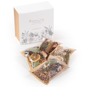 May include: A white rectangular box labeled Simmering Potpourri by Andallica with a botanical illustration, accompanied by four clear plastic pouches filled with dried botanicals including orange slices, cinnamon sticks, and pine needles.