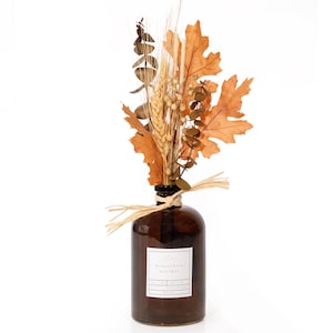 May include: A brown glass bottle with a bundle of dried wheat, leaves, and eucalyptus. The arrangement is tied with raffia and features a label that reads "Eucalyptus Harvest". The bottle is filled with a liquid.