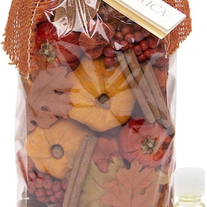 May include: A clear plastic bag filled with autumn-themed potpourri, including small pumpkins, cinnamon sticks, berries, and leaves. The bag is tied with a burlap ribbon and a tag that reads "ANDALLUCA". A small bottle of liquid sits beside the bag.
