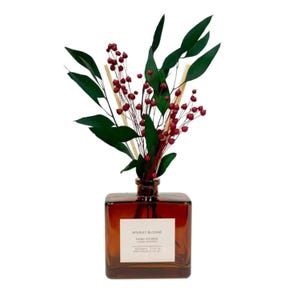May include: A brown glass diffuser bottle with a square shape, filled with green leaves, red berries, and wooden sticks. The label reads "Holiday Blooms, Hand Poured". The bottle is a decorative home fragrance item.