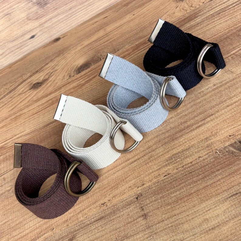 May include: Four fabric belts with metal D-ring buckles. The belts are in brown, black, grey, and white.