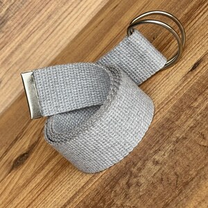 May include: A grey woven fabric belt with a silver metal buckle and two silver metal rings.