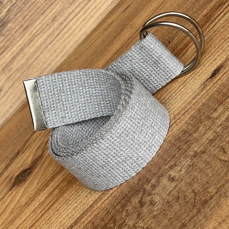 May include: A grey woven fabric belt with a silver metal buckle and two silver metal rings.