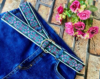 May include: A blue denim jean with a black and white patterned belt with a silver buckle. The belt has pink and blue accents.