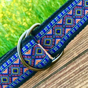 May include: A black dog collar with a colorful geometric pattern and a silver D-ring. The pattern features blue, pink, yellow, and black colors.