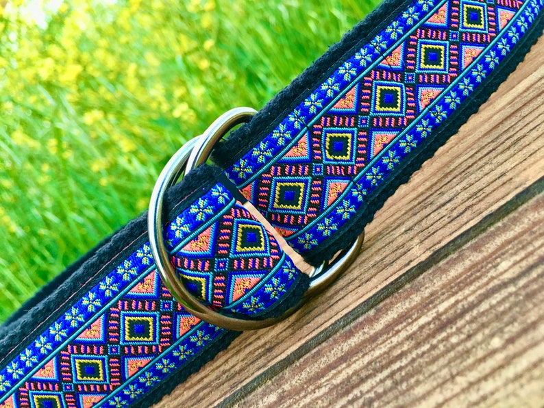 May include: A black dog collar with a colorful geometric pattern and a silver D-ring. The pattern features blue, pink, yellow, and black colors.
