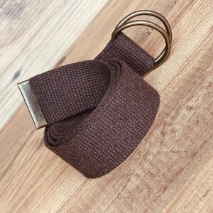 May include: A brown canvas belt with a double ring buckle. The belt is rolled up and the buckle is visible.