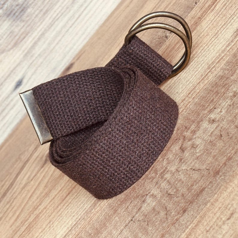 May include: A brown canvas belt with a double ring buckle. The belt is rolled up and the buckle is visible.