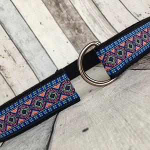 May include: A black dog collar with a blue, pink, and yellow geometric pattern. The collar has a silver metal D-ring.