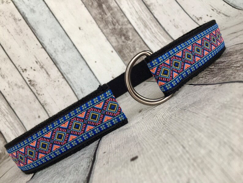 May include: A black dog collar with a blue, pink, and yellow geometric pattern. The collar has a silver metal D-ring.