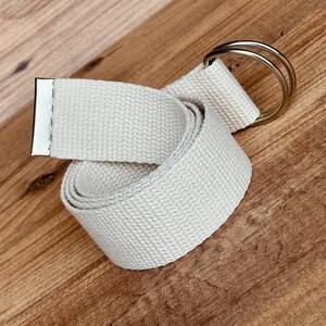 May include: A cream canvas belt with a silver double-ring buckle.
