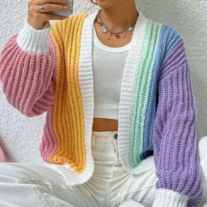 Può includere: Un cardigan a maglia a righe arcobaleno con maniche lunghe e scollo a V. Il cardigan è realizzato con un filato morbido e spesso e ha una vestibilità rilassata.
