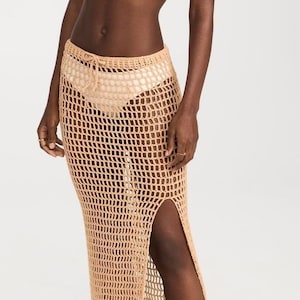 Puede incluir: Una falda larga de crochet beige con una abertura lateral y una cintura con cordón.