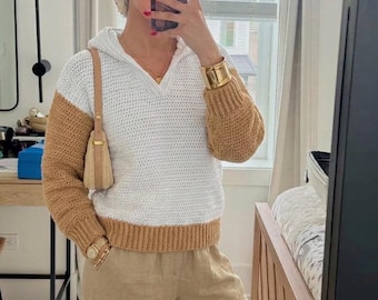 May include: A long-sleeve hooded sweater featuring a white torso and tan sleeves with a matching tan ribbed hem and cuffs. The sweater is paired with tan trousers and a small tan shoulder bag. The garment has a V-neckline and a textured knit pattern.