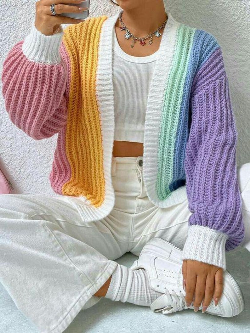 Peut inclure: Un cardigan en tricot ray&eacute; arc-en-ciel &agrave; manches longues et col en V. Le cardigan est fait d'un fil doux et &eacute;pais et a une coupe d&eacute;contract&eacute;e.