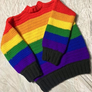 May include: A rainbow striped crocheted sweater with a mock neck and long sleeves. The sweater is made with different colored yarn in the order of red, orange, yellow, green, blue, purple, and black.