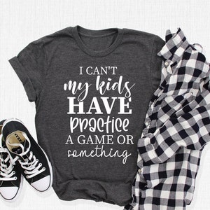 May include: A dark gray t-shirt with the text "I can't my kids have practice a game or something" printed in white.