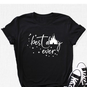 Puede incluir: Camiseta negra con texto blanco que dice "mejor d&iacute;a de todos" y una silueta blanca del castillo de Cenicienta.