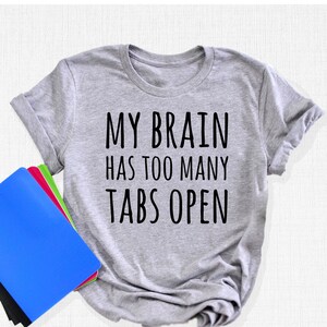 May include: Gray t-shirt with the text "MY BRAIN HAS TOO MANY TABS OPEN" printed in black.