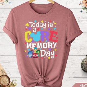 May include: A heather mauve t-shirt with a graphic design featuring the characters from the movie Inside Out. The text on the shirt reads "Today is a CORE MEMORY Day".