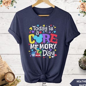 May include: A navy blue t-shirt with the text "Today is a CORE MEMORY Day" in colorful letters. The text is surrounded by small, colorful Mickey Mouse ears. The shirt features a graphic of the characters from the movie Inside Out.