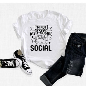 May include: White t-shirt with black text that reads "I'm not anti-social I'm just selectively social". The text is in a banner design with a black outline.