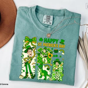 A light green t-shirt with a cartoon character design and text related to St. Patrick's Day, including a character holding a shamrock and the text "Happy St. Patrick's Day".