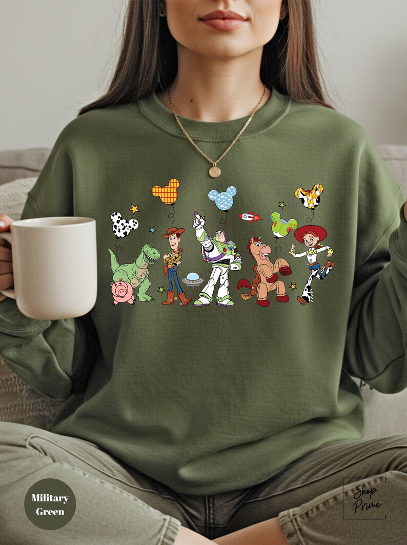 A woman wearing a green sweatshirt with a graphic of various cartoon characters from the Toy Story franchise, including Woody, Buzz Lightyear, and other beloved characters.