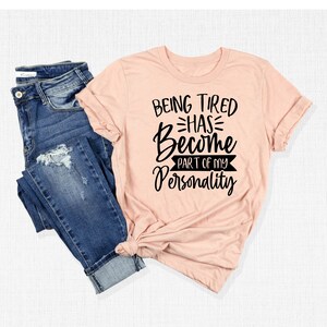 Może przedstawiać: R&oacute;żowy t-shirt z czarnym nadrukiem: "Bycie zmęczonym stało się częścią mojej osobowości".