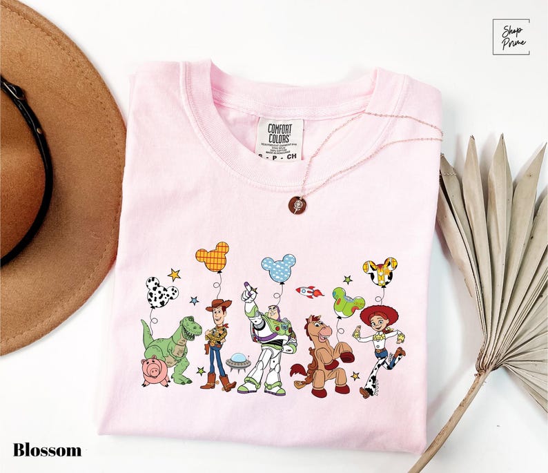 A pink t-shirt with a cartoon character design, including characters from the Toy Story franchise, such as Woody, Buzz Lightyear, and other beloved characters.