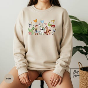 A person wearing a beige sweatshirt with a colorful graphic of various cartoon characters on it.