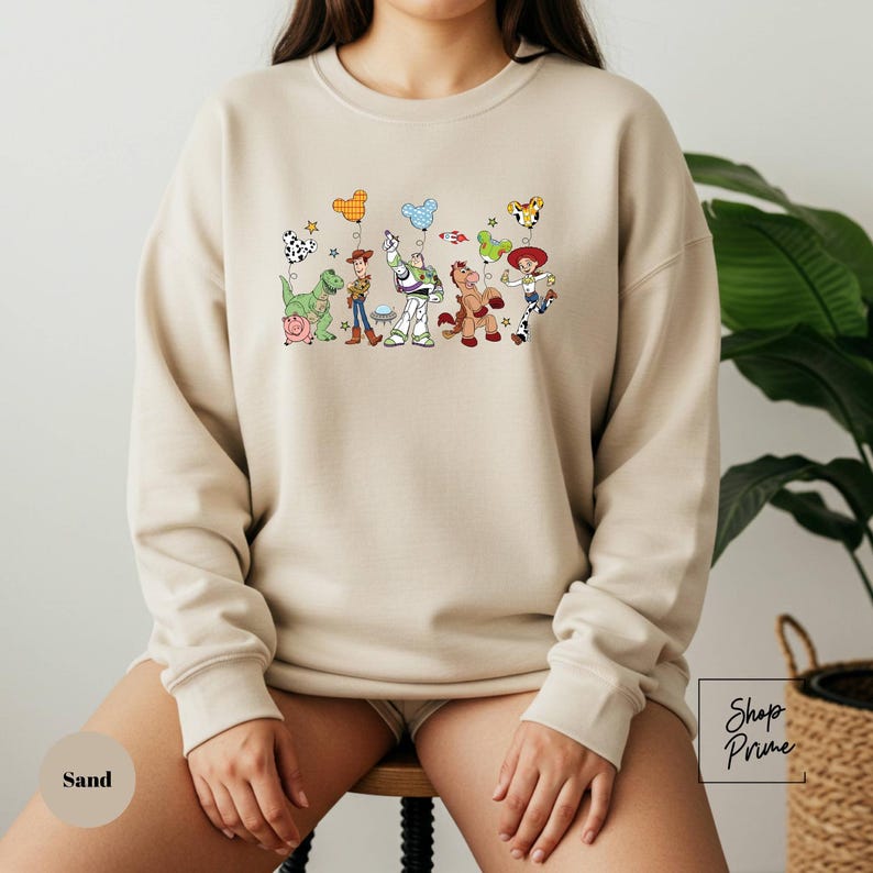 A person wearing a beige sweatshirt with a colorful graphic of various cartoon characters on it.