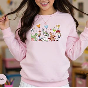 A woman wearing a pink sweatshirt with a cartoon character design on it.