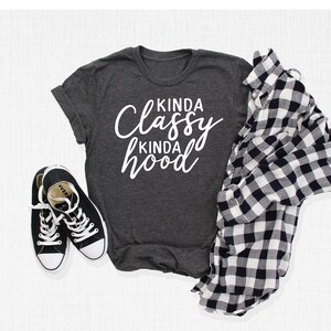 May include: A dark gray t-shirt with the text "Kinda Classy Kinda Hood" in white lettering.