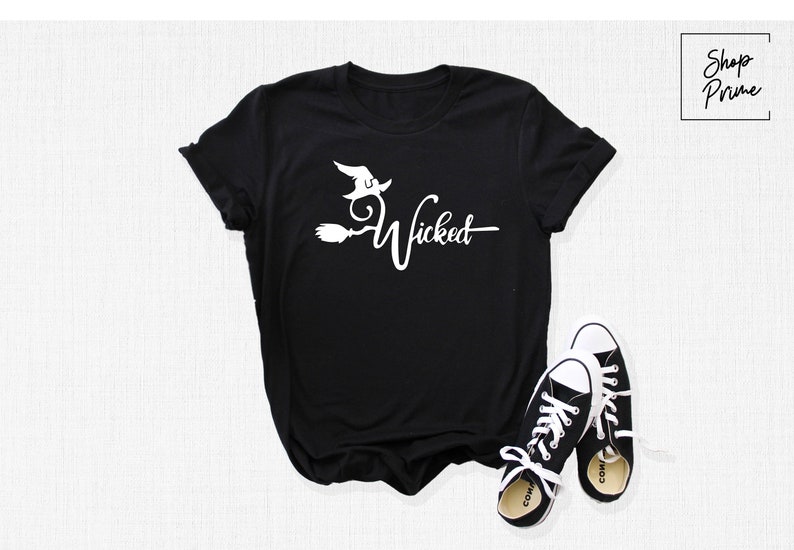 Puede incluir: Camiseta negra con un gr&aacute;fico blanco de una bruja volando en una escoba con el texto "Wicked".
