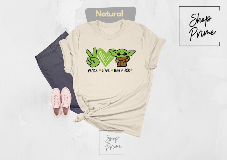 K&ouml;nnte beinhalten: Ein beiges T-Shirt mit einem gr&uuml;nen Peace-Zeichen, einem Herzen und einem Cartoon-Bild von Baby Yoda. Der Text auf dem Shirt lautet "Peace Love Baby Yoda".