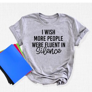 Pu&ograve; includere: Una maglietta grigia con la scritta "I wish more people were fluent in silence" stampata in nero.