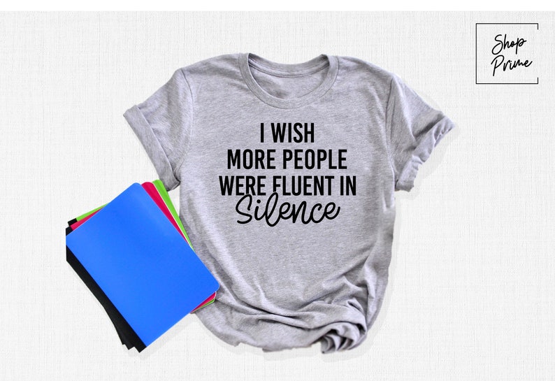 Pu&ograve; includere: Una maglietta grigia con la scritta "I wish more people were fluent in silence" stampata in nero.