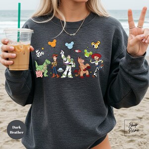 A woman is holding a drink and wearing a sweatshirt with a cartoon character design on it.