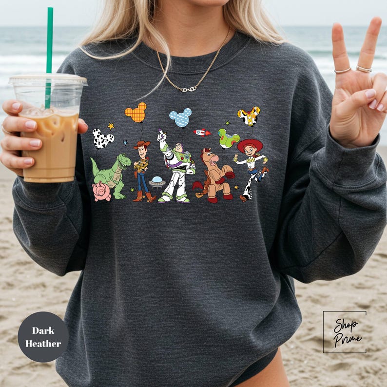 A woman is holding a drink and wearing a sweatshirt with a cartoon character design on it.