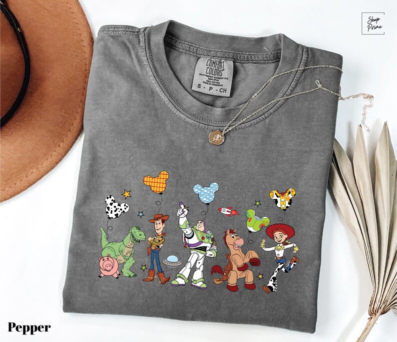 A gray t-shirt with a graphic of characters from the Toy Story movie, including Woody, Buzz Lightyear, and other beloved characters, along with various Disney-themed elements.