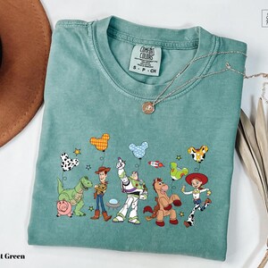 A light green t-shirt with a colorful graphic of characters from the Toy Story movie, including Woody, Buzz Lightyear, and other beloved characters.