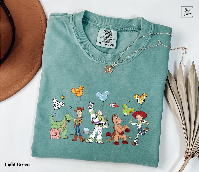 A light green t-shirt with a colorful graphic of characters from the Toy Story movie, including Woody, Buzz Lightyear, and other beloved characters.