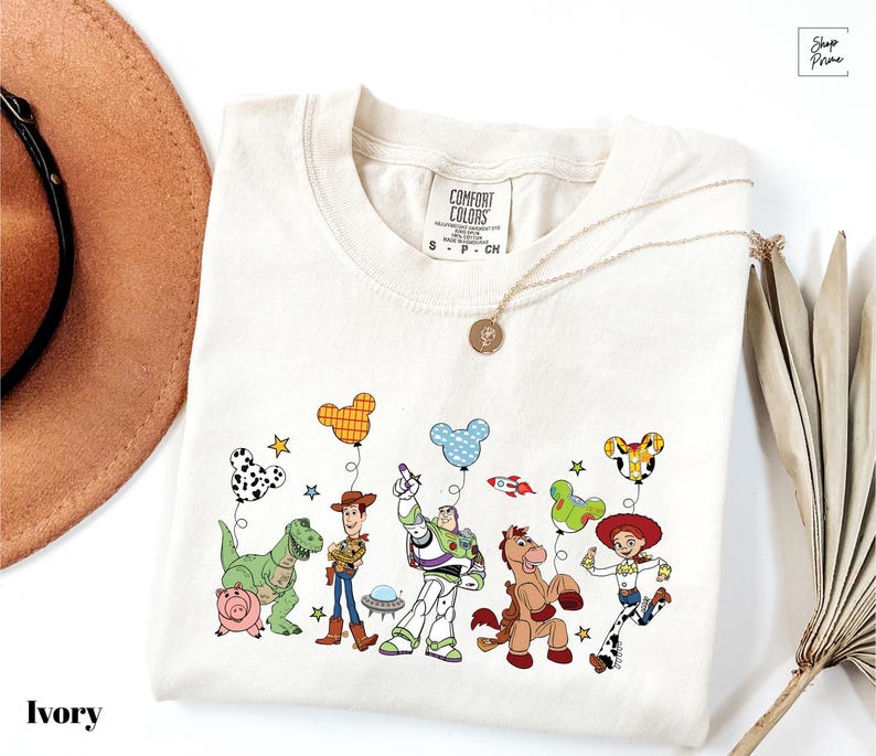 A white t-shirt with a cartoon illustration of various characters from the Toy Story franchise, including Woody, Buzz Lightyear, and other beloved characters.